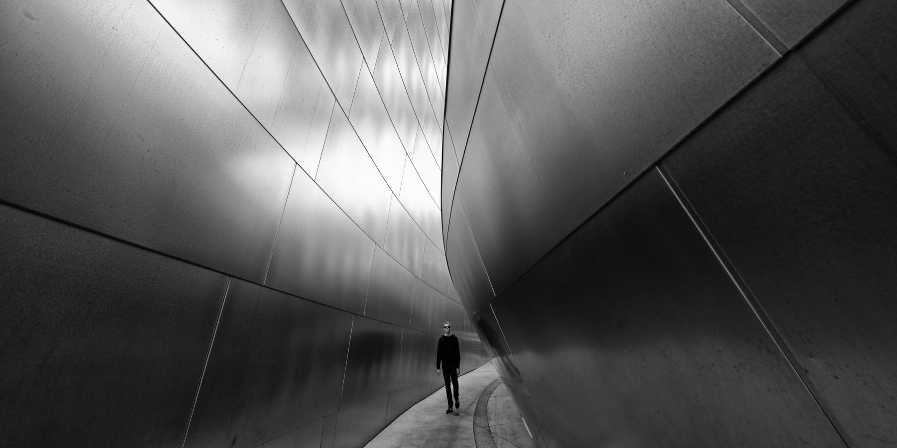 Homme qui se tient entre deux murs qui semblent tomber sur lui. Photo de Eric Forey.