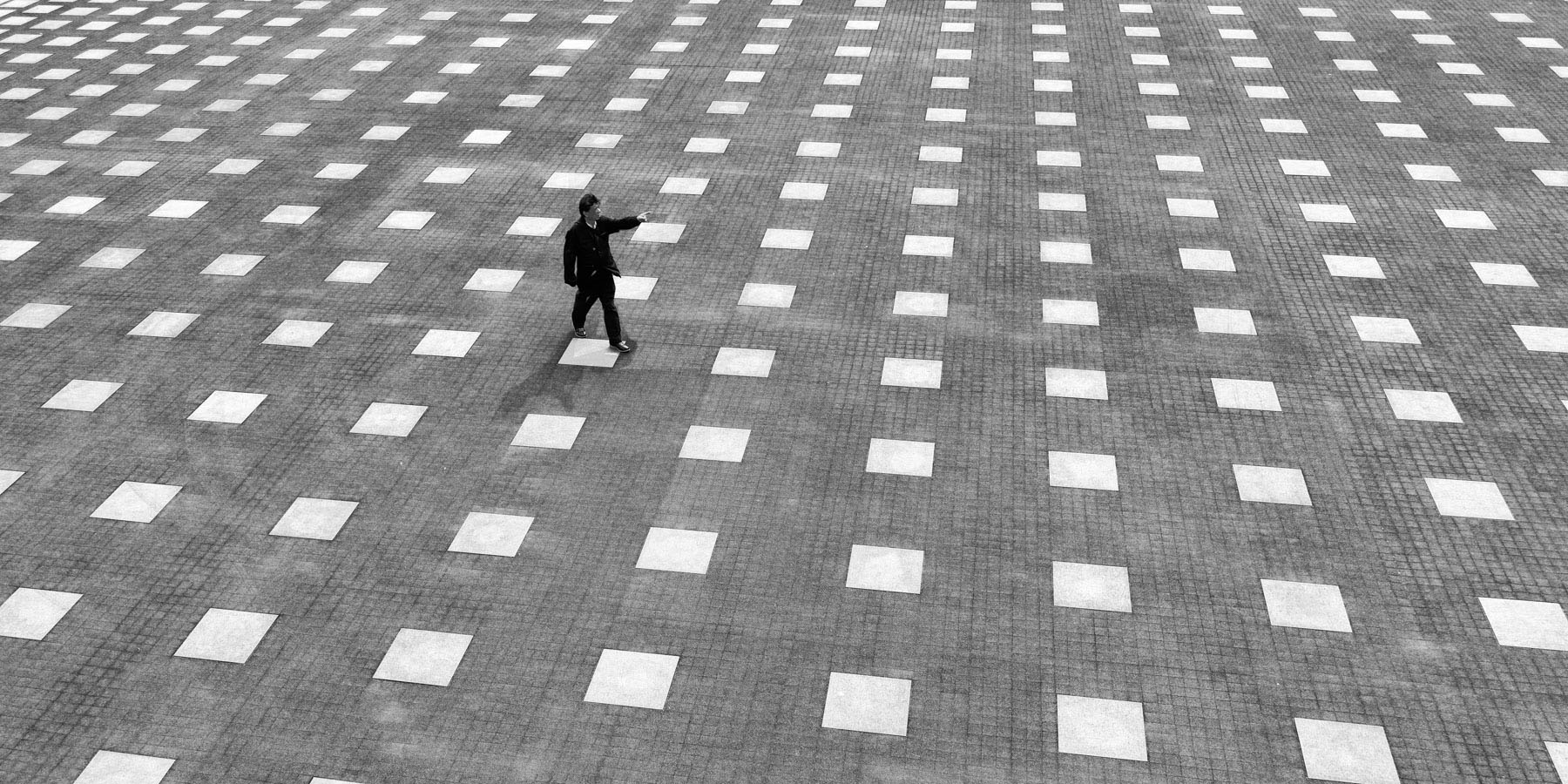 homme qui marche sur une place avec des carreaux noirs et blancs. Photo de Eric Forey